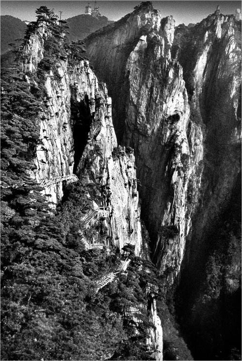 #171-019 On the left is a walkway built for tourists across the face of the cliff. China’s spectacular Huangshan National Park has many such paths made by workers who were suspended by ropes to drill holes for the horizontal supports. Over the years many improvements have been made in the park to make ever more spectacular areas accessible as China modernizes and promotes its tourism.